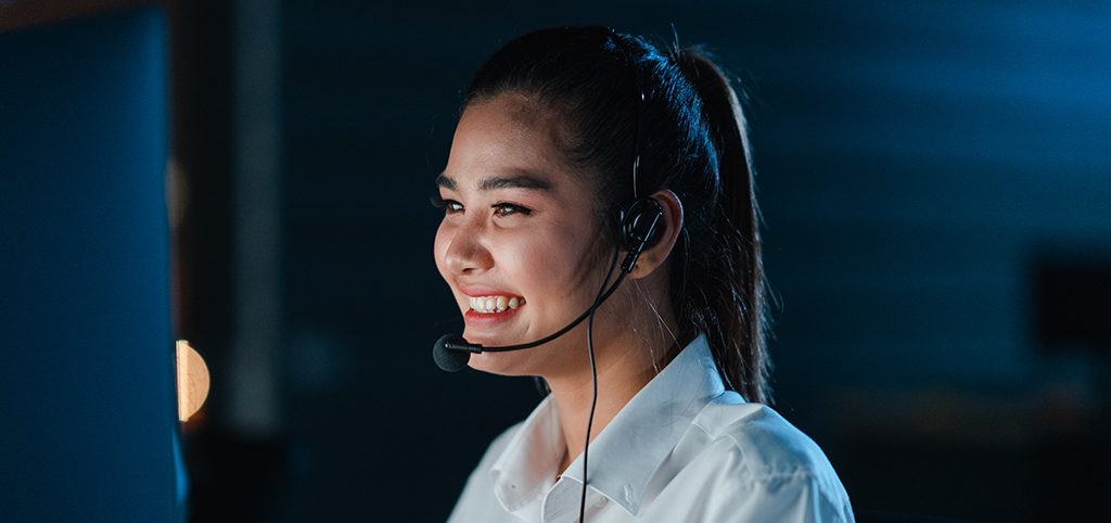 Millennial Asia young call center team or customer support service executive using computer and microphone headset working technical support in late night office. Telemarketing or sales job concept.