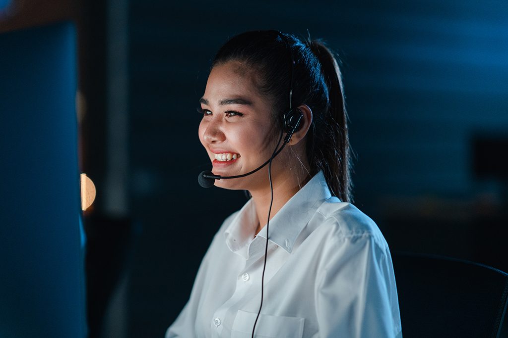 Millennial Asia young call center team or customer support service executive using computer and microphone headset working technical support in late night office. Telemarketing or sales job concept.