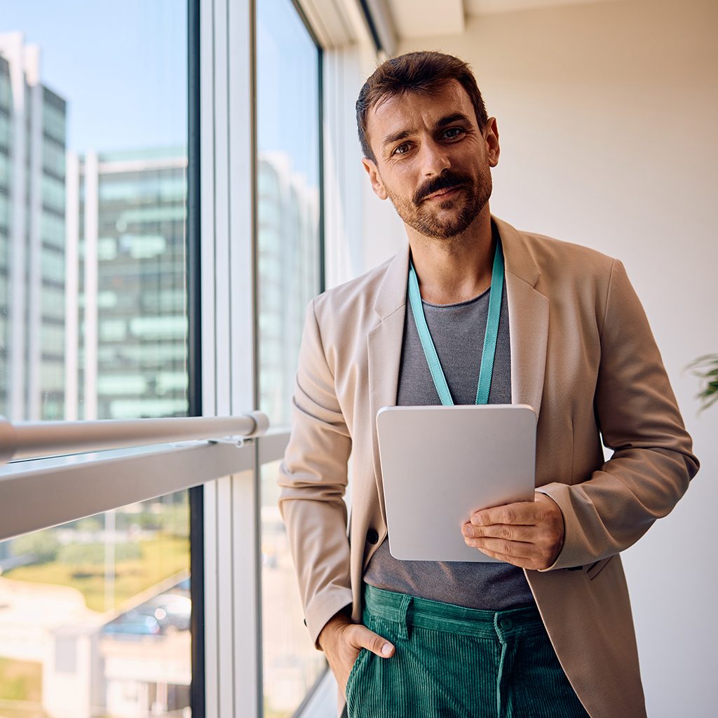 Smiling businessman working on digital tablet in the office and looking at camera. Copy space.